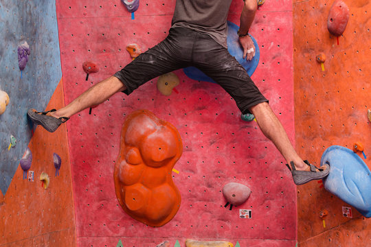 male climber training in bouldering gym wall, close up of leg muscles with shoes