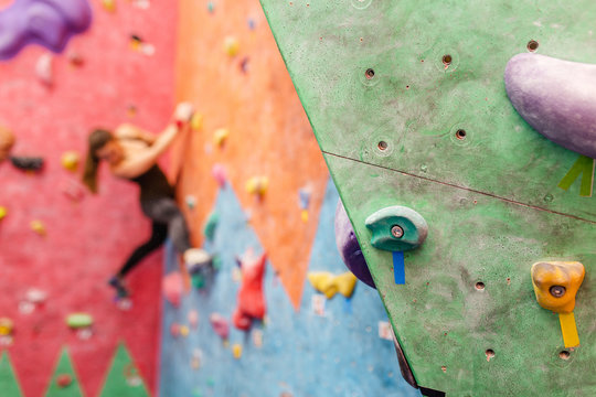 Blurred young woman climbing on an artificial rock wall indoors, bouldering concept