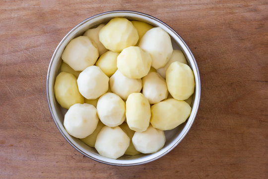 raw peeled potatoes in a circular bowl on an old rustic wooden table closeup, top view