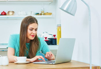 young woman working in kitchen area with laptop.