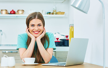 smiling woman with laptop working in kitchen area.