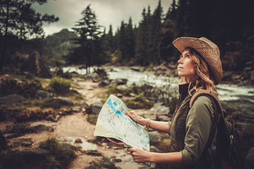 Fototapeta premium Woman hiker, searching right direction on map near wild mountain river