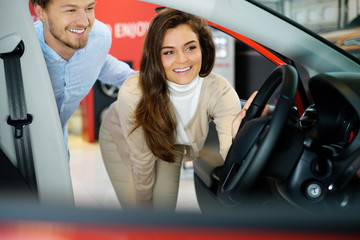 Beautiful young couple looking a new car at the dealership showroom