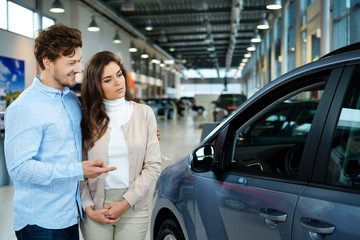 Beautiful young couple looking a new car at the dealership showroom