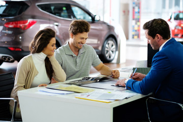 Beautiful young couple reading a booklet at the dealership showroom