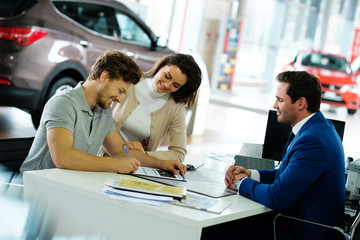 Beautiful young couple signs documents at dealership showroom