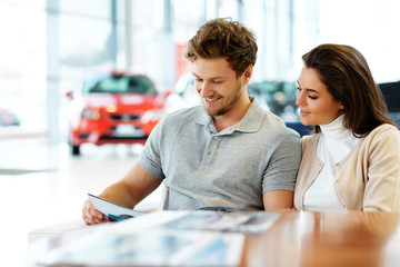 Obraz premium Beautiful young couple reading a booklet at the dealership showroom