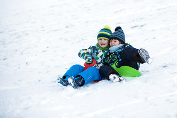 Two kids, boy brothers, sliding with bob in the snow, wintertime
