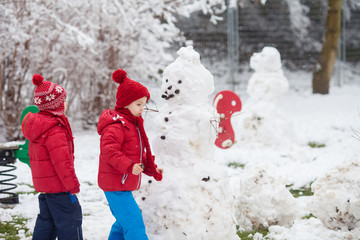 Happy beautiful children, brothers, building snowman in garden