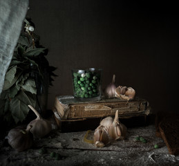 rustic still life, vintage. green peas, old books, garlic, flour on a wooden table. dark background