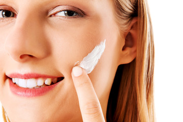 Portrait of young woman applying moisturizer cream on her pretty face