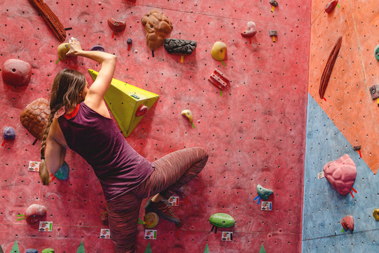 Young strength woman extreme bouldering in a modern rock climbing gym indoors