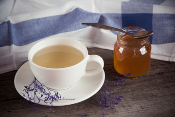 Green tea in a white cup and jar of honey with spoon and blue ki