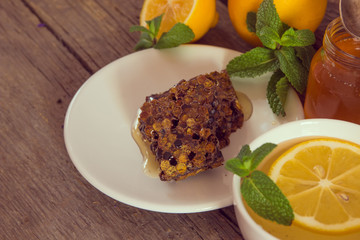 Honeycomb, honey in jar, green tea, lemon with leaf and mint on