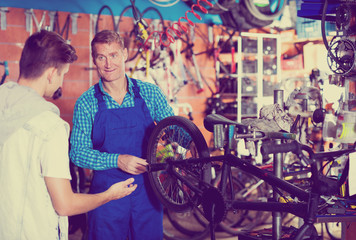 Obraz na płótnie Canvas Man working with bicycles wheel and helping boy