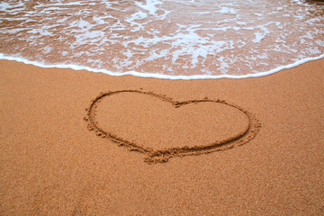 Heart drawn in the sand and waves background. Valentines day. Sy