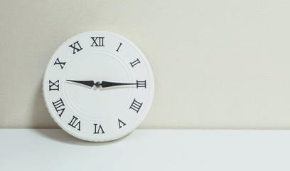 Closeup white clock for decorate show a quarter past nine or 9:15 a.m. on white wood desk and cream wallpaper textured background with copy space