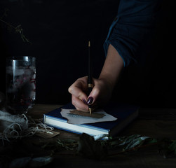 female hand writes a note on the old wooden table. dark backgrounds. vintage.