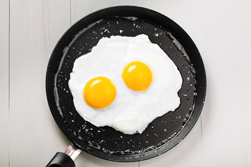 Fried eggs for delicious healthy easy breakfast on a table. Fresh homemade meal on a frying pan. Traditional breakfast food. International cuisine food.  Top view.