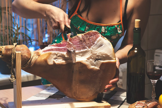 Woman Hands Slises Spanish Jamon Serrano On Wooden Tabla Jamonera. Bottle And Glass Of Red Wine. Selective Focus. Home Cooking, Food Photo Concept.