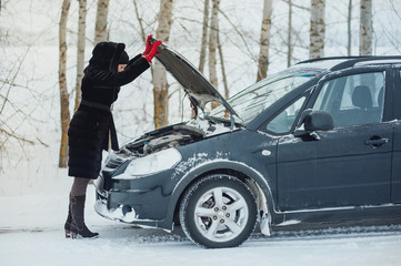 girl looks under cowl of broken car on rural road