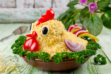 Salad shaped rooster on a plate on a wooden table