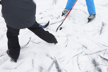 A group of children playing ice hockey at the skating rink outside in winter.