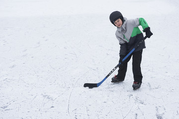 Naklejka premium Child boy playing ice hockey at the skating rink outside in winter.