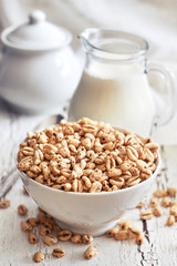 Puffed wheat cereal in white bowl with pitcher of milk in background