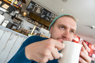 Man drinking coffee in the early Morning at a cafe and looking through the window