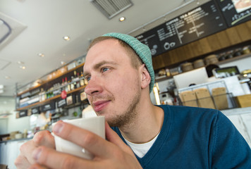 Man drinking coffee in the early Morning at a cafe and looking through the window