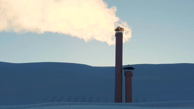 A lot of smoke from the chimney on the roof of the house on a cold day in winter