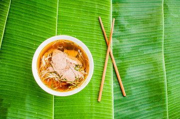 A bowl of Traditional Vietnamese beef soup Pho Bo on banana leaf background. © galitskaya