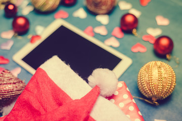 Defocused mobile tablet computer with Santa Claus hat and Christmas decoration. Online shopping background.