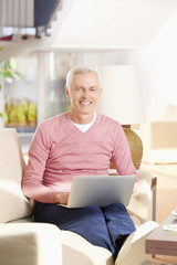 Shot of a senior man using his laptop and working from home while sitting on living room.