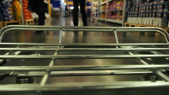 Big supermarket shopping cart in motion goes between blurred shelves