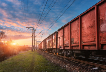 Railway station with cargo wagons and train against sunny sky with clouds in the evening. Colorful...