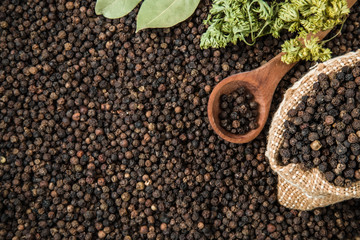 Black pepper grain in the burlap bag on the pepper background with dried bay leaves and parsley. Composition of seasoning. Healthy eating and lifestyle.