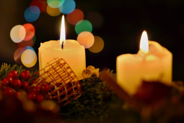 Detail of two burning candles with background made of colorful bokeh lights placed on the Christmas tree as a symbol of peaceful and serene holiday time 