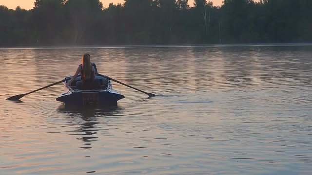 A loving couple riding on a rowing boat on the river in time of golden sunset. The golden light of the sun on the water surface of the lake. Golden sunset sunrise on the lake.