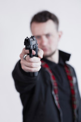 Closeup of focused young man standing and aiming with gun