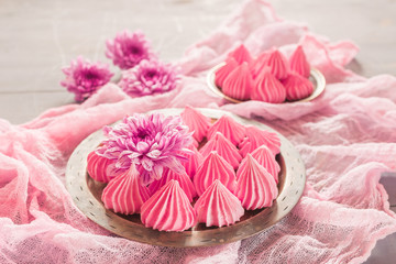 Air meringue with fresh flowers lie on a metal dish on a pink ve