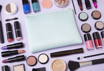 A selection of cosmetic beauty products arranged around a blue make up bag on a pastel purple background