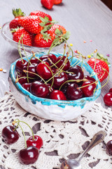 Red ripe strawberries in the glass bowl and cherries in pottery