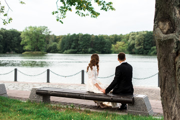 happy bride and groom at a park on their wedding day sitting on a bench near the lake