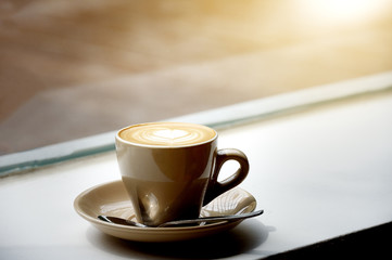 Coffee cup of hot latte art near window.