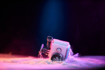 Concept: gear, gadget, action lifestyle, millennial. Vivid colorful shot of action camera in waterproof case fall dropped in powder sand. Time freeze.