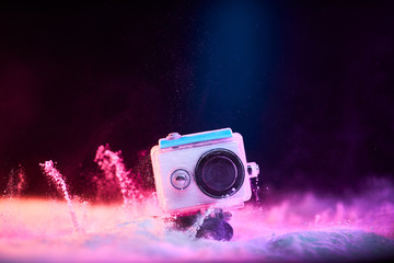 Naklejka premium Concept: gear, gadget, action lifestyle, millennial. Vivid colorful shot of action camera in waterproof case fall dropped in powder sand. Time freeze.
