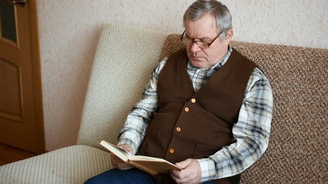 Old man sitting on the couch at home reading a book