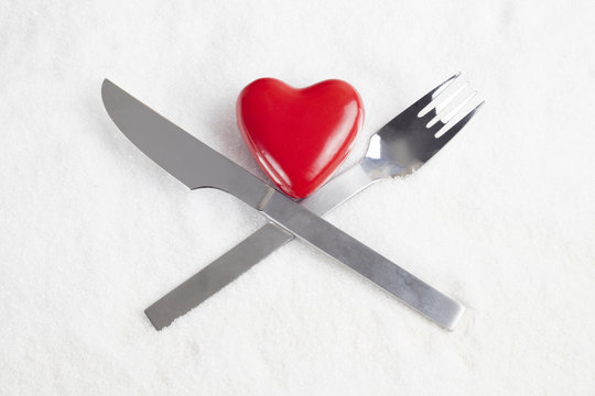 Shape of red heart with crossed fork and knife in snow white background